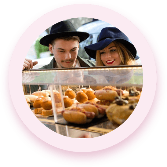 A man and woman looking at pastries in a display case.